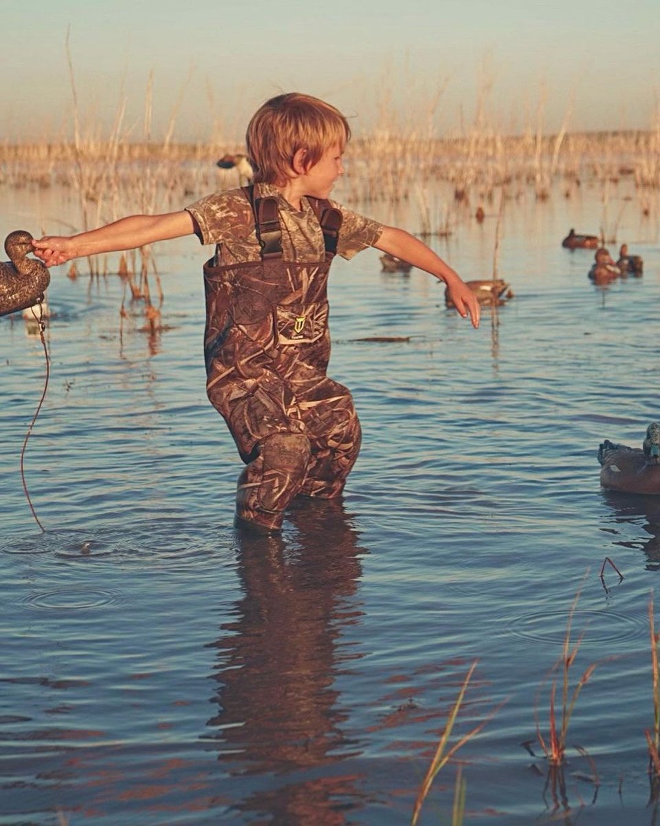 Kid in hunting gear inside of a pond