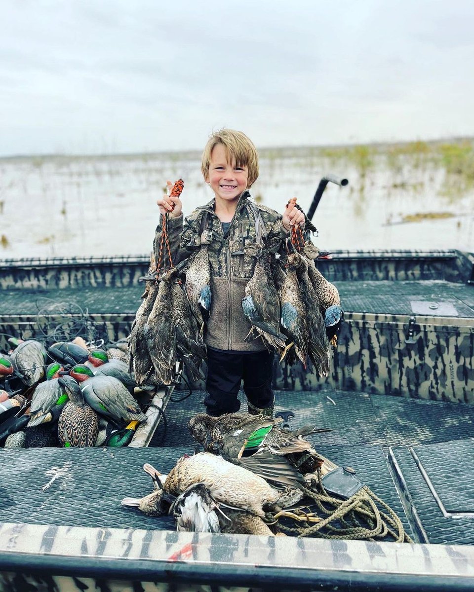 Kid in hunting gear holding hunted ducks