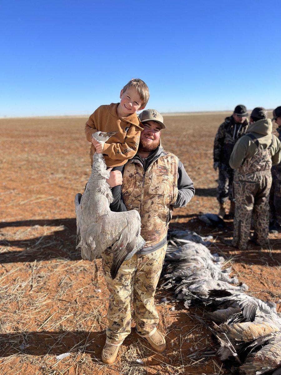 Male hunter holding a kid who is holding a deceased sandhill crane